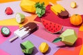 Origami ice cream and handmade cardboard fruits on multicolored paper.