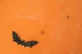 An origami paper bat on an orange studio background with spiders and cobwebs.