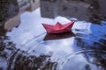 Origami paper boat in a puddle of rain water. The photo illustrates cloudy weather: rain, flood