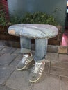 An original chair in the shape of legs. Creative sitting in nature - jeans and sneakers. Street stool next to the sidewalk. Turkey