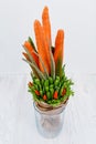 An original vegetable bouquet consisting of carrots, pea pods, lettuce leaves, red pepper and aloe is stand in a glass vase on a w