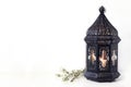 Ornamental black Moroccan, Arabic lantern with blooming prunus tree branches on white table. Greeting card for Muslim