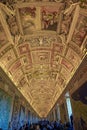 ornamental ceiling with religious figures in one of the corridors of the vatican museum with countless tourists watching.