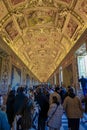 ornamental ceiling with religious figures in one of the corridors of the vatican museum with countless tourists watching.