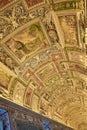 ornamental ceiling with religious figures in one of the corridors of the vatican museum with countless tourists watching.