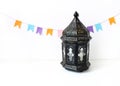 Ornamental dark Moroccan, Arabic lantern on the white table. Party decoration, string of colorful paper flags. Greeting