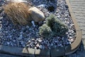 Ornamental flower bed with perennial pine and gray granite boulders, mulched bark and pebbles in an urban setting near the parking