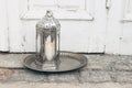 Ornamental Moroccan lantern on silver tray standing on stone ground. Old shabby door in background. Greeting card