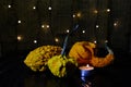 Ornamental pumpkins and burning candle on background of blurry garland lights.