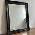 Ornate black-framed mirror leaning against a white wall. The frame features intricate Royalty Free Stock Photo