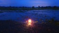 An ornate lantern glowing in the evening after sunset. On the ground, reflected in flood waters in a field on a winters evening.