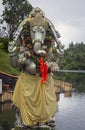 An ornate statue of an Indian god standing on the shore of a lake