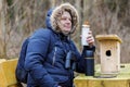 Ornithologist drinking tea in park near wooden bird cage