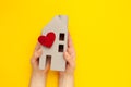 Orphanage. Figure of a house with a heart in his hands on a yellow background. Nursing home concept Royalty Free Stock Photo