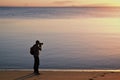 Photographer in silhouette taking photographs on a beach at sunset