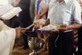 Orthodox christian priest showering golden wedding rings on white pillow with holy water, sacred religious ritual in church at