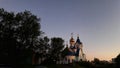 Orthodox Church on the background of the sunset sky. Dark outlines of trees and bushes. Lights are shining. Golden domes glisten i