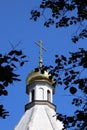 Orthodox cross and dome against a background of blue sky framed by tree branches