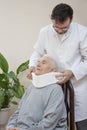 The orthopedic surgeon puts on a white orthopedic collar of a very old woman sitting on a chair.