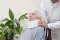 The orthopedic surgeon puts on a white orthopedic collar of a very old woman sitting on a chair.