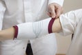 Orthopedic surgeon in a white coat assumes a stabilizer on the woman`s elbow.
