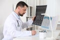 Orthopedist examining X-ray picture at desk in clinic