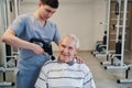 Orthopedist using percussion massager on aged male shoulder