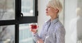 ortrait of young pensive woman standing by window with cup of tea