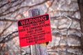 Red sign posted on pole reads warning buried fiber optic cable - bokeh background of winter trees - Royalty Free Stock Photo