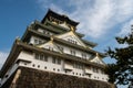 Osaka Castle majestic main tower with green traditional roofs and gold cravings, seen from below, Osaka, Japan.