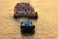 Osaka, Japan - July 25, 2023: Tug boat pulls crowded barge down river with golden glow on water