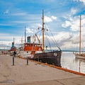 A large image of an old steamer, with a large black pipe, shabby sides, standing at the pier in the port