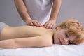 The osteopath works with the spine. A teenage child lies on a couch in front of a doctor. A chiropractor examines the