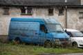 The abandoned wreck of a blue Mercedes-Benz Sprinter van overgrown by grass causing an environmental problem