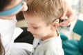 Otolaryngologist putting hearing aid in little boy's ear indoors