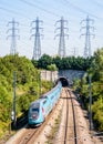 A Ouigo TGV Duplex high-speed train is entering a tunnel under a row of transmission towers Royalty Free Stock Photo