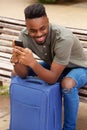 Oung african american man sitting with mobile phone and suitcase Royalty Free Stock Photo