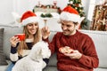 oung hispanic couple wearing christmas hat drinking coffee and eating cookies