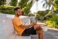 oung hispanic man wearing casual clothes sitting on a bench using his mobile phone smiling.