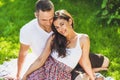 Ouple in love sitting on a picnic blanket outdoor. Caucasian happy dreamy man and smiling woman sitting on green grass in park. Royalty Free Stock Photo