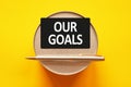 OUR GOALS - words on a black sheet on a yellow background with round metal stand and metal writing pen. Business, finance and Royalty Free Stock Photo