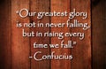 Our greatest glory is not in never falling, but in rising every time we fall. Inspirational quote on vintage wooden background.