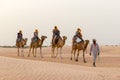 Tourists ride on camels guided by a local man, in the Sahara desert, Tunisia, Africa