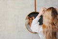 out of focus a blonde in a white shirt looks at her reflection in a round mirror