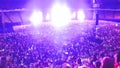 Out of focus image of big crowd of fans sitting on stadium seats watching and listening rock concert at night.