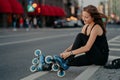 Sideways shot of active woman sits on road adjustes rollerblades prepares for skating puts on inline skates has hair Royalty Free Stock Photo