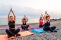 Outdoor activity at sea coast. Side view of group of Caucasian women meditate sitting on sports mats on pebble beach Royalty Free Stock Photo