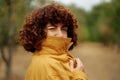 Attractive winking curly girl covering face with jacket. Autumn season concept