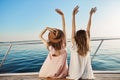 Outdoor back shot of two young female on luxury vacation, waving at seaside while sitting on yacht. Best friends are Royalty Free Stock Photo