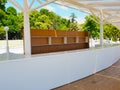 An outdoor bar with empty shelves and a white bar against a backdrop of green trees and palm trees